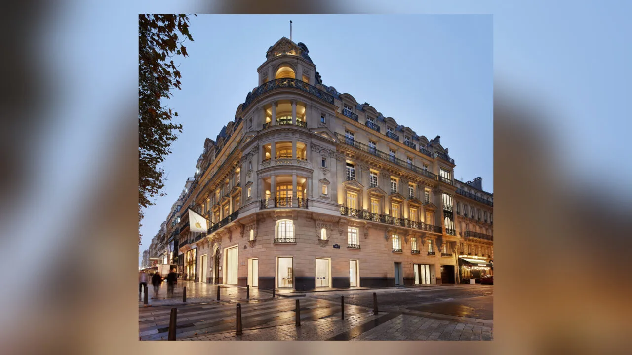 Einer der Apple Stores in Frankreich: die Filiale an den Champs-Élysées in Paris in einem beleuchteten Eckgebäude mit Apple-Flagge am Abend.