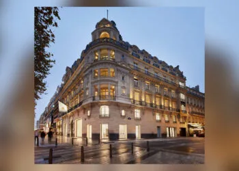 Einer der Apple Stores in Frankreich: die Filiale an den Champs-Élysées in Paris in einem beleuchteten Eckgebäude mit Apple-Flagge am Abend.