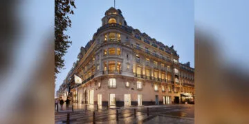 Einer der Apple Stores in Frankreich: die Filiale an den Champs-Élysées in Paris in einem beleuchteten Eckgebäude mit Apple-Flagge am Abend.