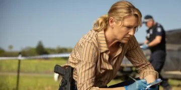 Szenenbild aus Dustfall bei Apple TV: Anna Torv als Ermittlerin Tig Pollard kniet mit Notizblock und Handschuhen an einem abgesperrten Tatort, im Hintergrund ein Polizist