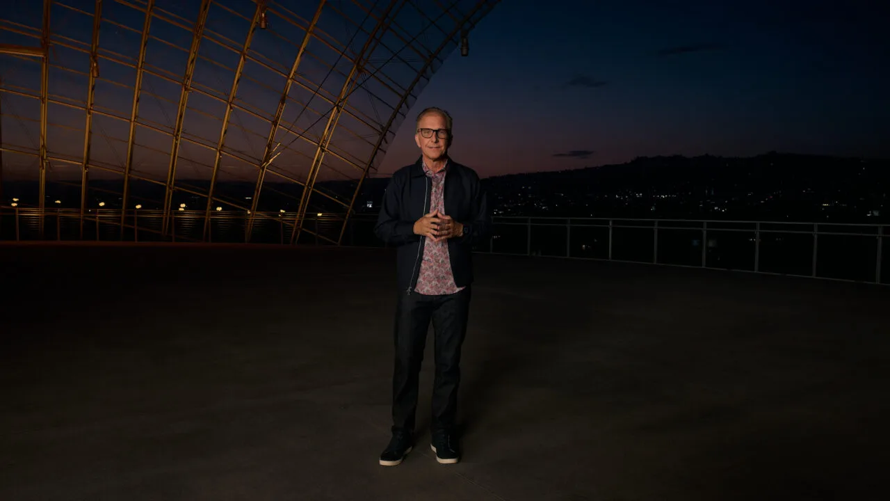 Greg Joswiak, Apples Marketingchef, steht in der Abenddämmerung auf einer Terrasse unter einer geschwungenen Stahl-Glas-Konstruktion