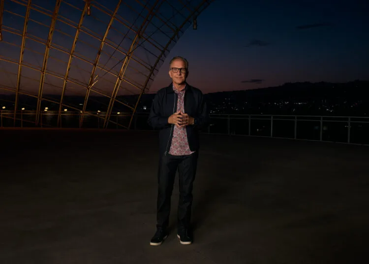 Greg Joswiak, Apples Marketingchef, steht in der Abenddämmerung auf einer Terrasse unter einer geschwungenen Stahl-Glas-Konstruktion