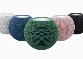 HomePod mini 2 in Weiß, Blau, Grün, Rosa und Mitternacht im Halbkreis, vorn das grüne Modell mit leuchtender Oberseite