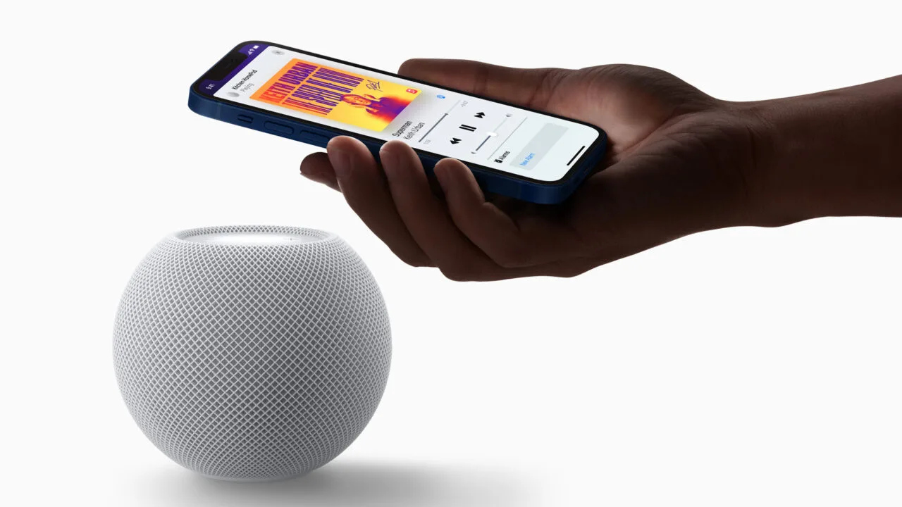 HomePod mini Siri AI: weißer HomePod mini, darüber eine Hand mit iPhone, das die Musikwiedergabe auf dem Lautsprecher anzeigt