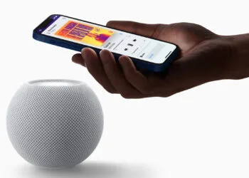 HomePod mini Siri AI: weißer HomePod mini, darüber eine Hand mit iPhone, das die Musikwiedergabe auf dem Lautsprecher anzeigt
