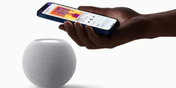 HomePod mini Siri AI: weißer HomePod mini, darüber eine Hand mit iPhone, das die Musikwiedergabe auf dem Lautsprecher anzeigt