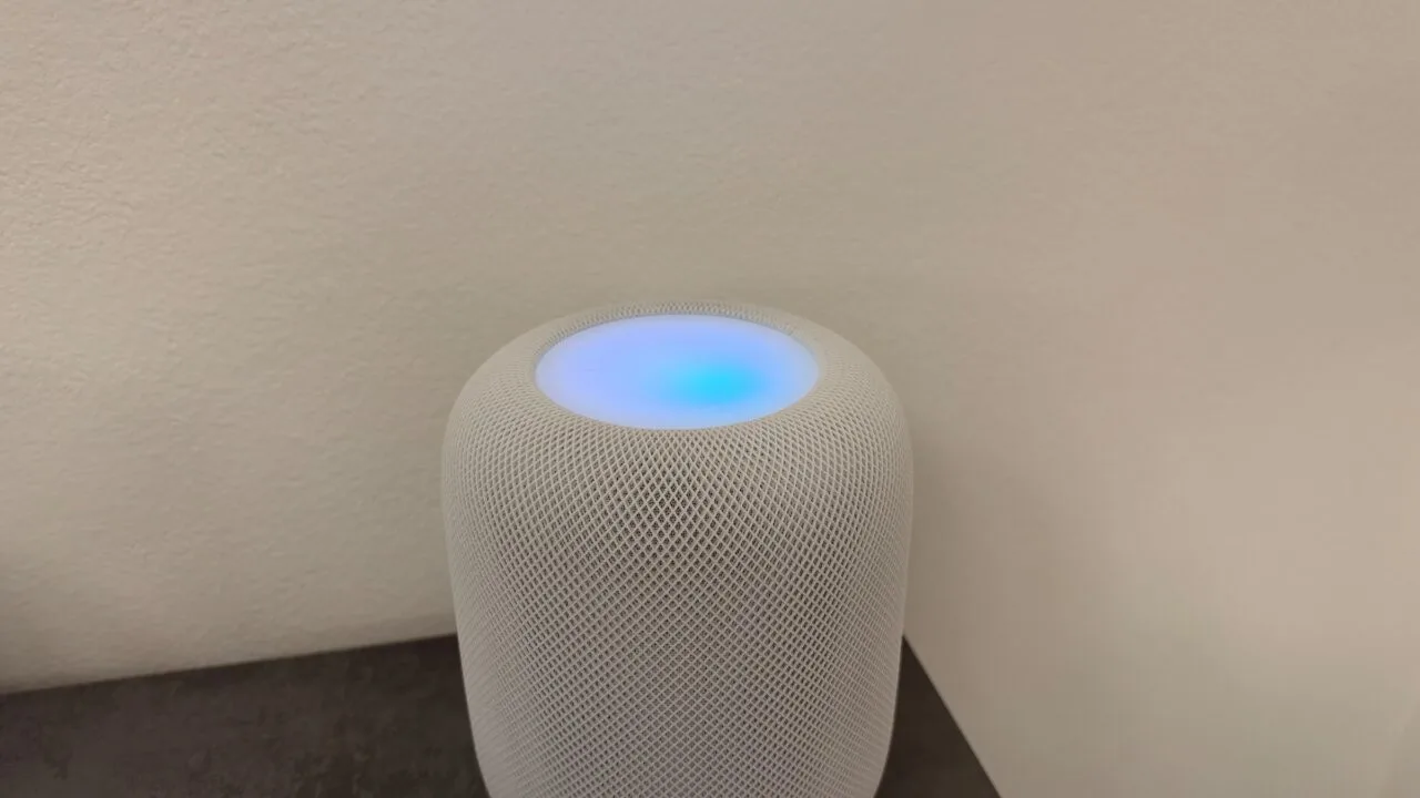 Weißer HomePod mit leuchtender Oberseite in Blau- und Violetttönen vor einer hellen Wand – so sieht HomePod Sound-Leuchten aus