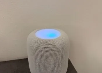 Weißer HomePod mit leuchtender Oberseite in Blau- und Violetttönen vor einer hellen Wand – so sieht HomePod Sound-Leuchten aus