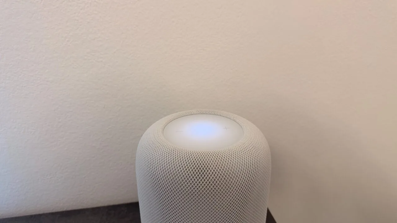 HomePod Touch sperren: weißer HomePod mit leuchtender Touch-Fläche und Plus- und Minus-Symbolen vor einer hellen Wand
