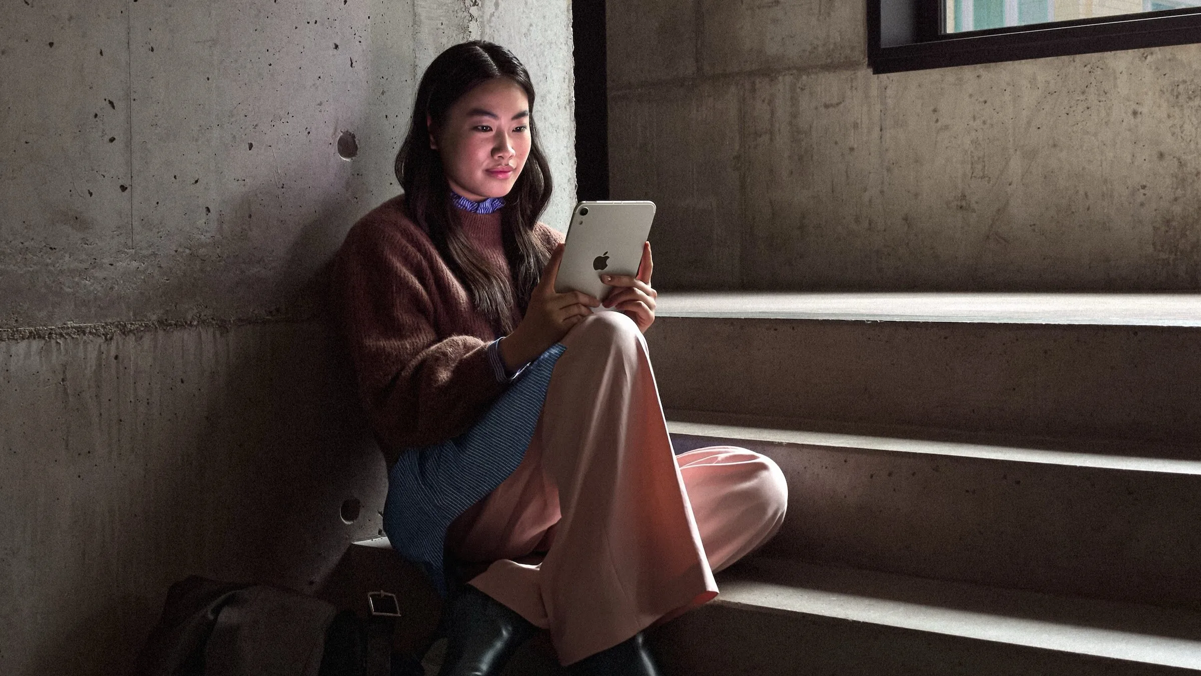 Szene aus Apples Vorstellung des iPad mini A20 Pro: Eine Frau sitzt in einem dämmrigen Treppenhaus und liest auf dem iPad mini