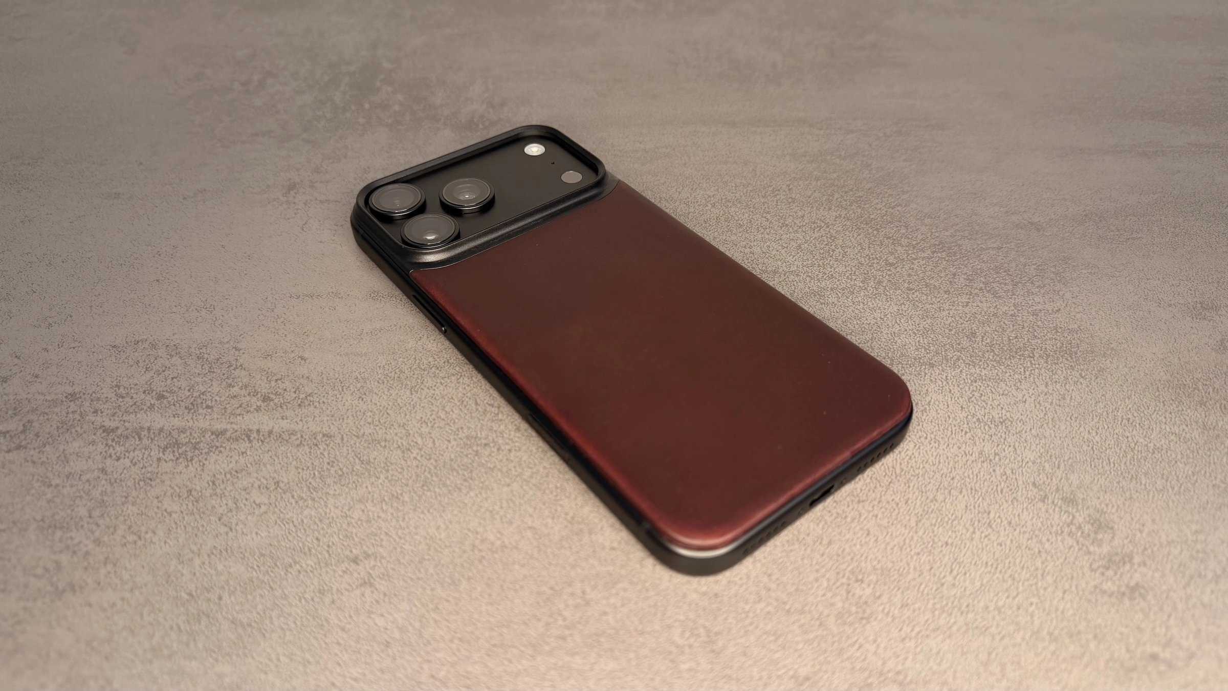 Nomad Hüllen iPhone 18 Pro: Mag Leather Back in Burgundy auf der Rückseite eines schwarzen iPhone, auf grauem Untergrund