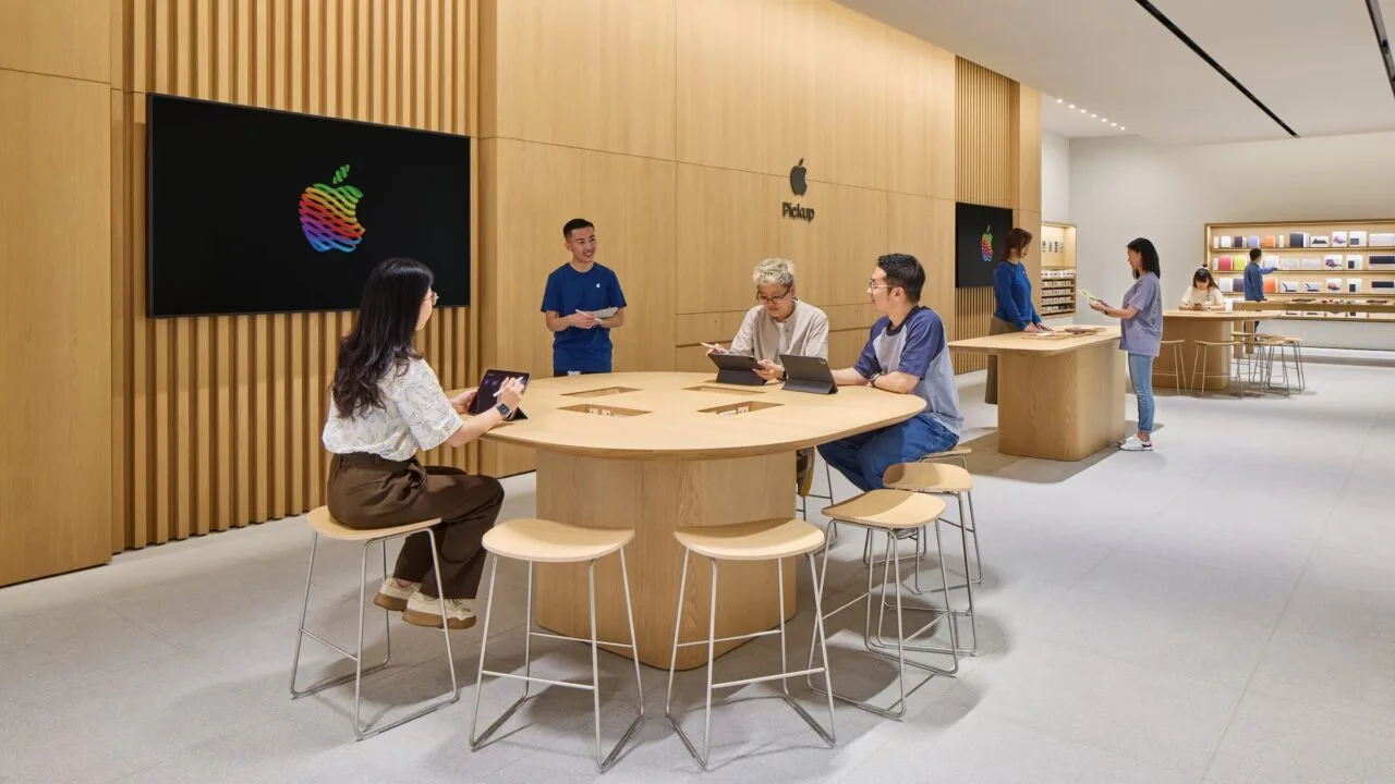 Symbolbild zu iPhone China: Apple Store mit Holzwänden, an einem Tisch arbeiten Kunden mit iPads, daneben ein Mitarbeiter