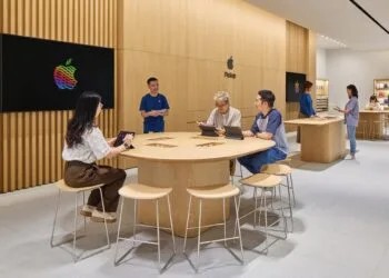 Symbolbild zu iPhone China: Apple Store mit Holzwänden, an einem Tisch arbeiten Kunden mit iPads, daneben ein Mitarbeiter