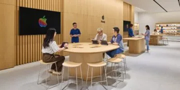 Symbolbild zu iPhone China: Apple Store mit Holzwänden, an einem Tisch arbeiten Kunden mit iPads, daneben ein Mitarbeiter