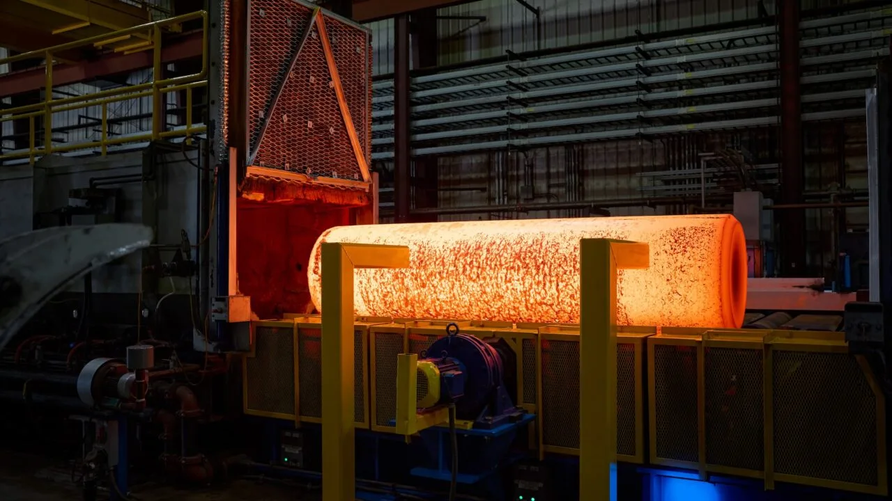 iPhone Duo Titan USA: glühender Metallblock nach dem Austritt aus einem Industrieofen in einer Werkhalle, davor gelbe Stützen