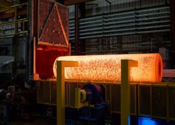 iPhone Duo Titan USA: glühender Metallblock nach dem Austritt aus einem Industrieofen in einer Werkhalle, davor gelbe Stützen