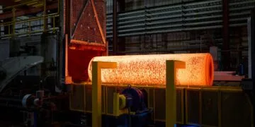 iPhone Duo Titan USA: glühender Metallblock nach dem Austritt aus einem Industrieofen in einer Werkhalle, davor gelbe Stützen