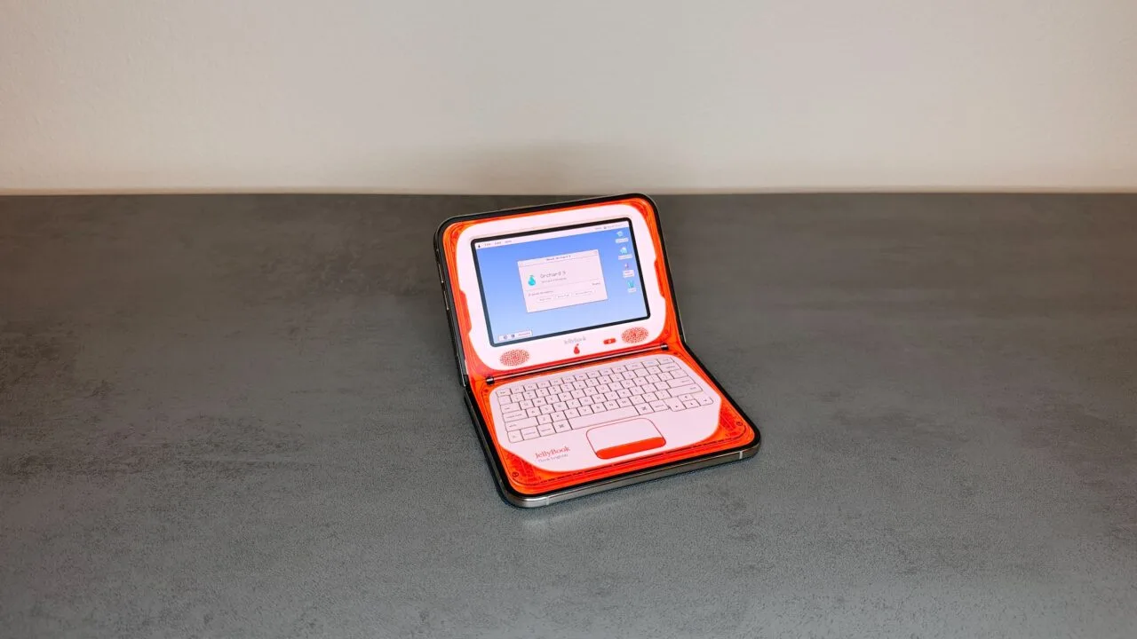 Eine der angepassten iPhone Duo Apps verwandelt das halb aufgeklappte iPhone Duo auf einem Tisch in einen orangefarbenen Retro-Laptop mit Bildschirm oben und Tastatur unten.