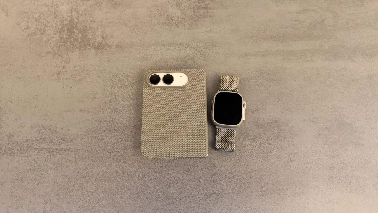 iPhone Duo mit Apple Watch entsperren: zugeklapptes iPhone Duo in einer Hülle mit Blick auf die Kamera neben einer Apple Watch Ultra mit Milanaise-Armband auf grauer Steinoberfläche