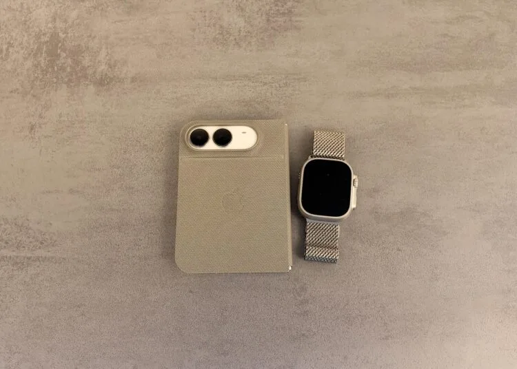 iPhone Duo mit Apple Watch entsperren: zugeklapptes iPhone Duo in einer Hülle mit Blick auf die Kamera neben einer Apple Watch Ultra mit Milanaise-Armband auf grauer Steinoberfläche