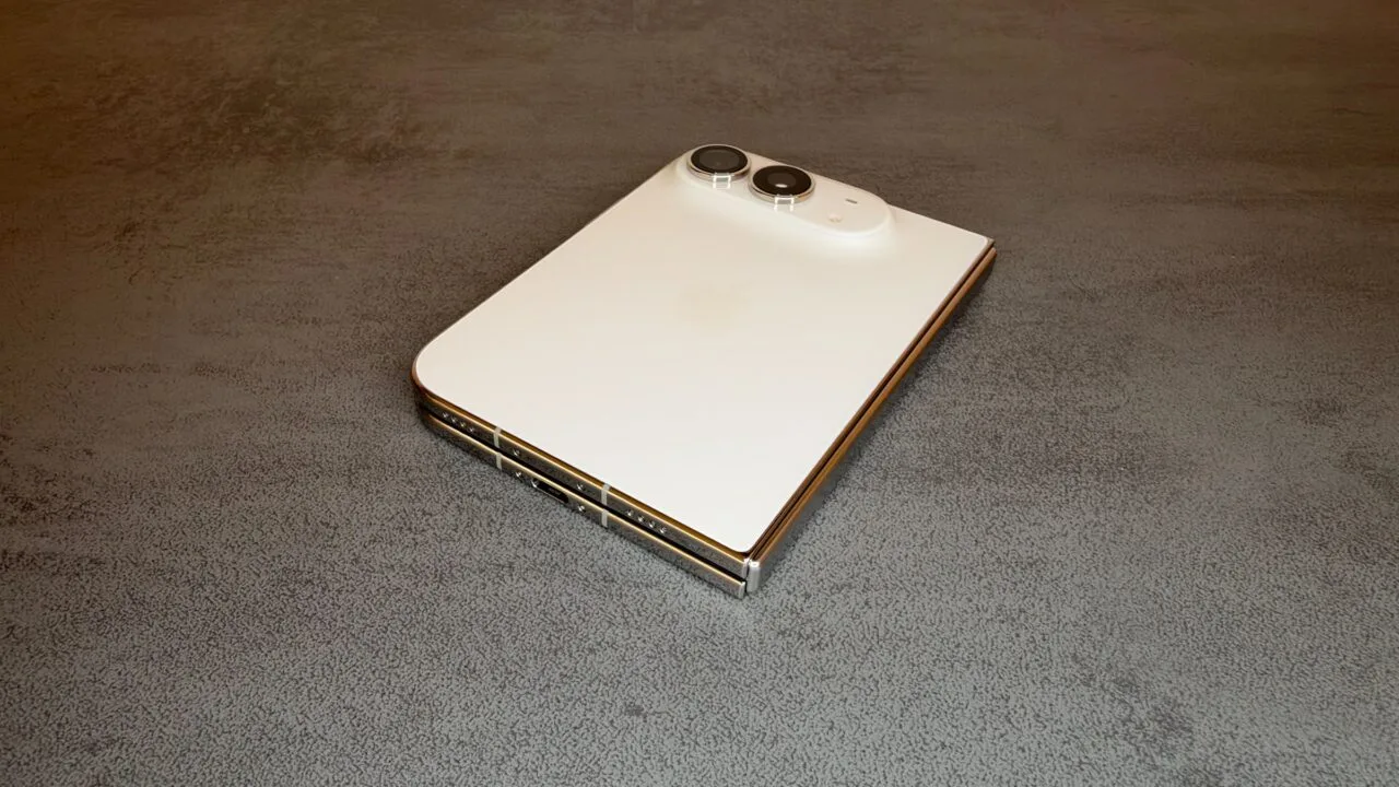 Zum iPhone Duo Reparaturhandbuch: das zugeklappte iPhone Duo in Sternenweiß auf einem Tisch, mit Rückglas, Kamera, Scharnier und USB-C-Anschluss.