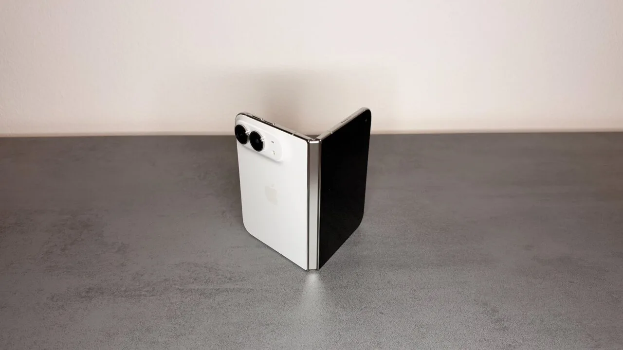 iPhone Duo Scharnier: weißes iPhone Duo halb aufgeklappt und wie ein Buch auf einer grauen Steinoberfläche aufgestellt, das silberne Scharnier zeigt zur Kamera