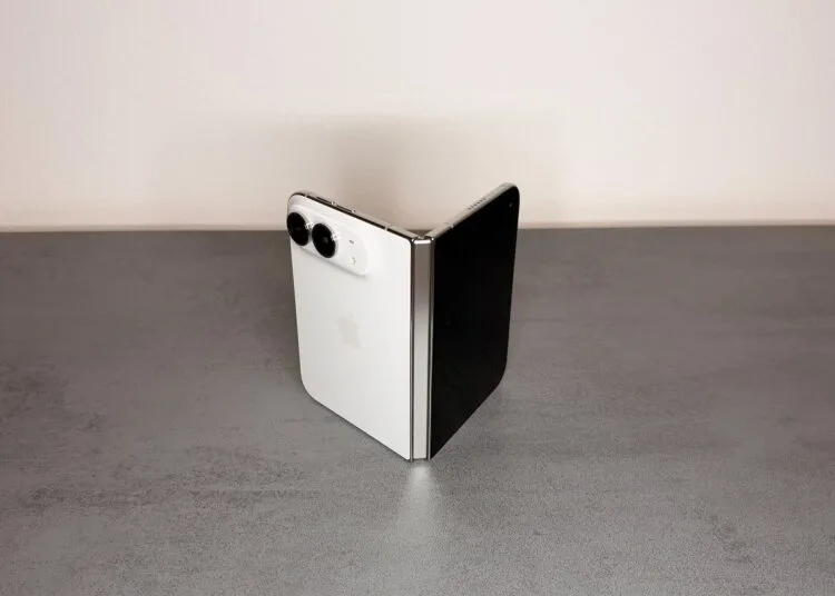 iPhone Duo Scharnier: weißes iPhone Duo halb aufgeklappt und wie ein Buch auf einer grauen Steinoberfläche aufgestellt, das silberne Scharnier zeigt zur Kamera