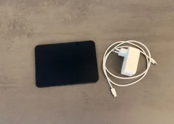 iPhone Duo schnell laden: aufgeklapptes iPhone Duo auf einer grauen Steinoberfläche, daneben ein weißes USB-C-Netzteil und ein geflochtenes USB-C-Ladekabel