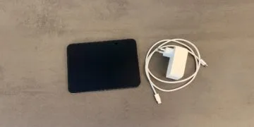 iPhone Duo schnell laden: aufgeklapptes iPhone Duo auf einer grauen Steinoberfläche, daneben ein weißes USB-C-Netzteil und ein geflochtenes USB-C-Ladekabel