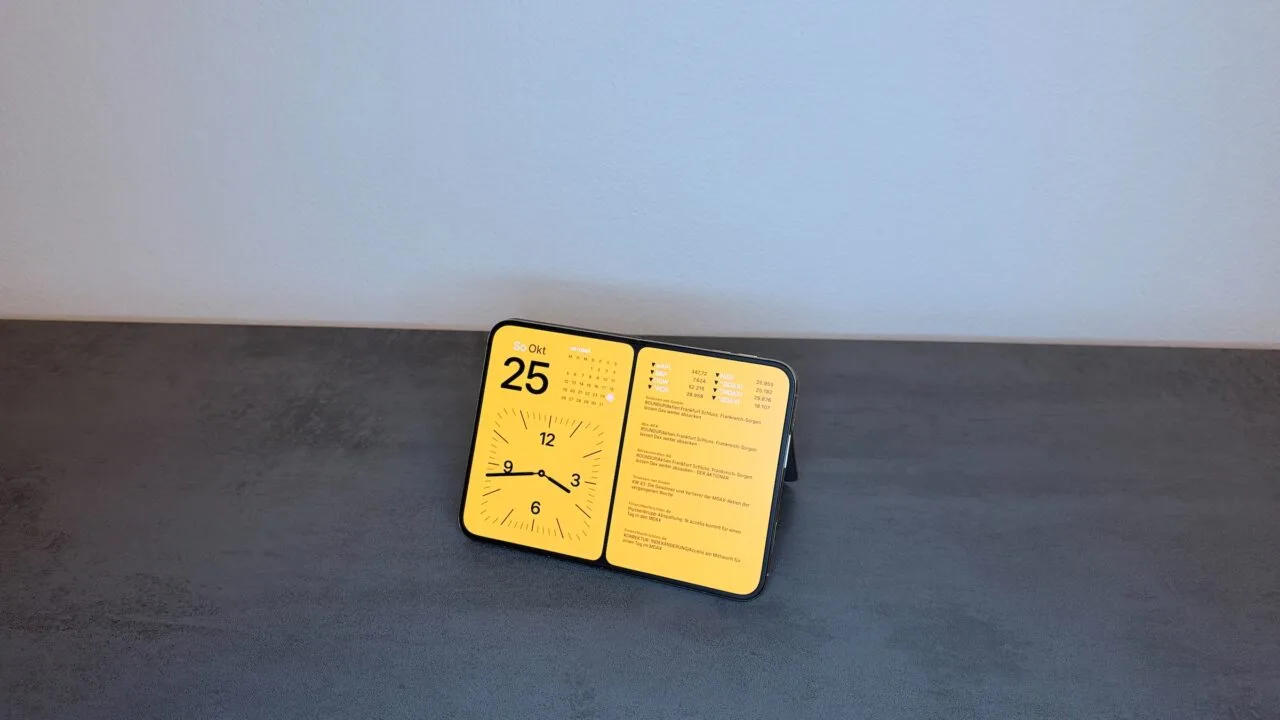 iPhone Duo Standby am Standfuß: Das ganz aufgeklappte iPhone Duo steht angewinkelt im Querformat und zeigt Datum, Kalender, Uhr und Aktienkurse.