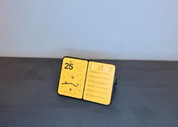 iPhone Duo Standby am Standfuß: Das ganz aufgeklappte iPhone Duo steht angewinkelt im Querformat und zeigt Datum, Kalender, Uhr und Aktienkurse.