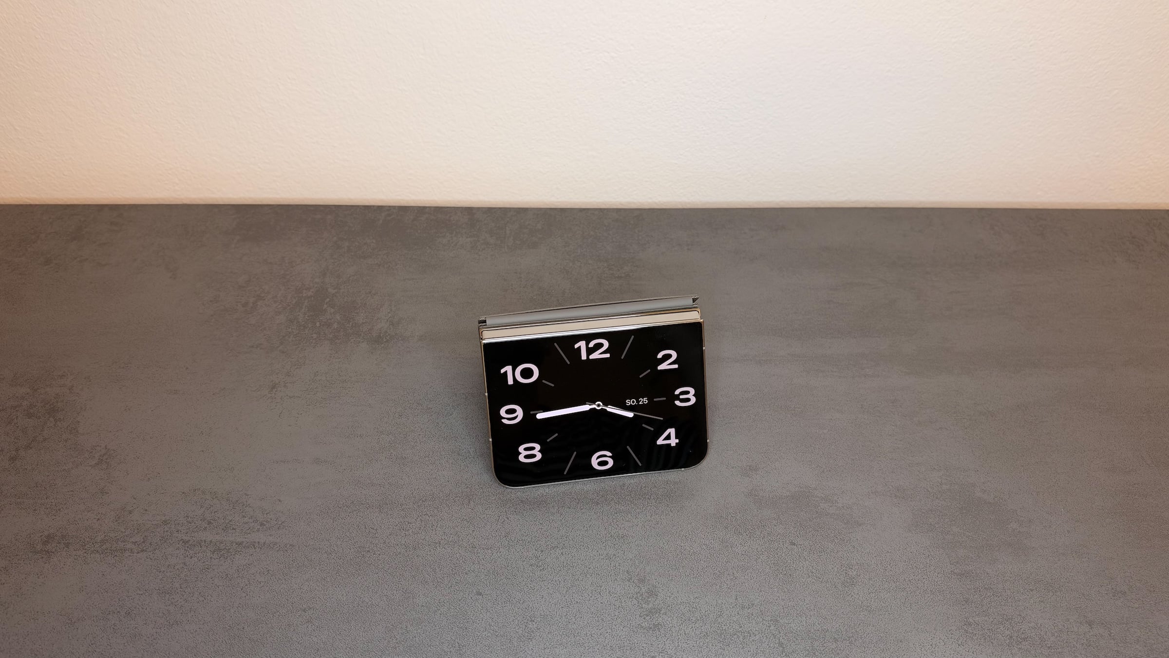 iPhone Duo StandBy in tent position: the iPhone Duo set up as a tent shows an analog clock with the date on its outer display.