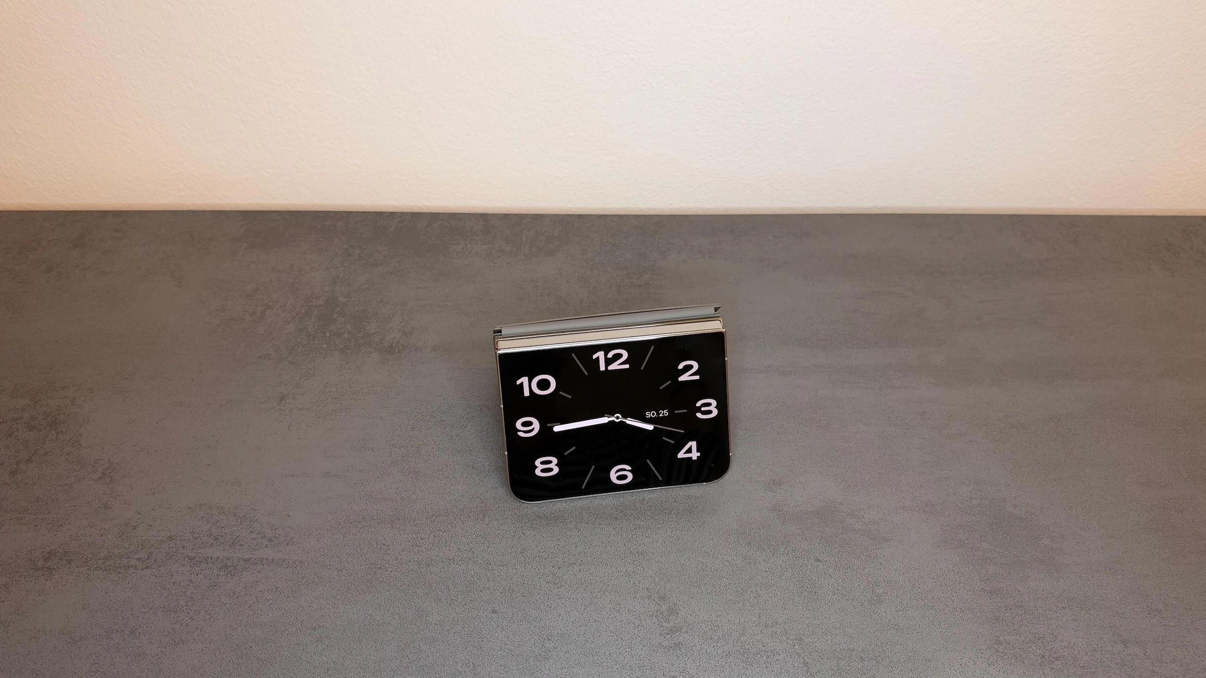 iPhone Duo Standby im Zelt: Das als Zelt aufgestellte iPhone Duo zeigt auf dem äußeren Display eine analoge Uhr mit Datum.