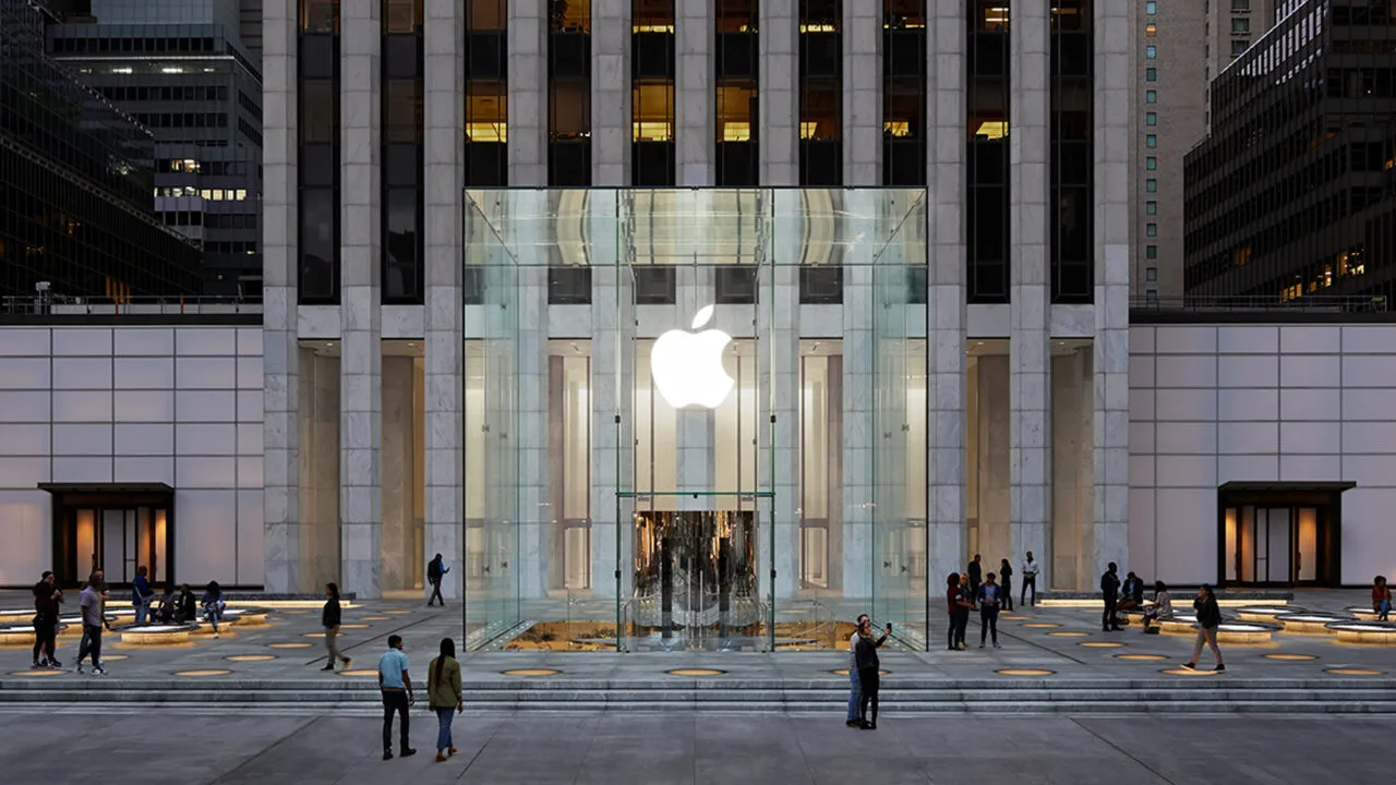 Der Apple Store an der Fifth Avenue in New York, der mehr als 150 iPhone Duo Vorführgeräte bekommen soll: Glaswürfel mit leuchtendem Apple-Logo vor dem Hochhaus in der Abenddämmerung
