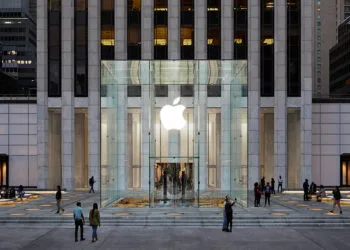 Der Apple Store an der Fifth Avenue in New York, der mehr als 150 iPhone Duo Vorführgeräte bekommen soll: Glaswürfel mit leuchtendem Apple-Logo vor dem Hochhaus in der Abenddämmerung
