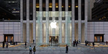 Der Apple Store an der Fifth Avenue in New York, der mehr als 150 iPhone Duo Vorführgeräte bekommen soll: Glaswürfel mit leuchtendem Apple-Logo vor dem Hochhaus in der Abenddämmerung