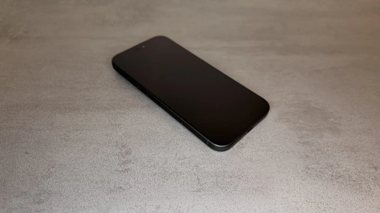 iPhone ohne Rahmen: schwarzes iPhone 18 Pro Max mit flachem Display und sichtbarem Seitenrahmen schräg von oben auf grauer Steinplatte