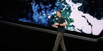 Ein Apple-Manager präsentiert auf der Bühne vor einem riesigen Gerätebildschirm mit farbigem Muster – Archivbild zum erwarteten Start des MacBook Pro mit Touchscreen