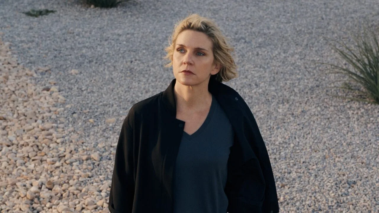 Pluribus Staffel 2: Rhea Seehorn als Carol Sturka steht in schwarzer Jacke auf einer Kiesfläche mit Wüstenpflanzen, Szene aus der ersten Staffel