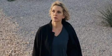 Pluribus Staffel 2: Rhea Seehorn als Carol Sturka steht in schwarzer Jacke auf einer Kiesfläche mit Wüstenpflanzen, Szene aus der ersten Staffel