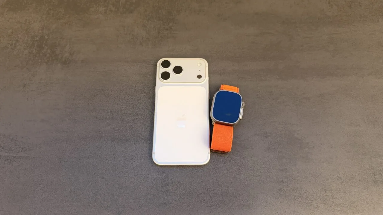 Taptic Engine Patentstreit: iPhone in Weiß mit Dreifachkamera von hinten, daneben eine Apple Watch Ultra mit orangefarbenem Alpine Loop auf grauem Untergrund