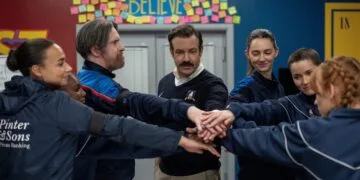 Ted Lasso Staffel 5: Ted Lasso legt mit dem Frauenteam von AFC Richmond die Hände zusammen, darüber das Believe-Schild